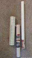 Photo showing three different paper rolls on a carpeted floor: a tall white roll, a baking parchment roll with label, and a transparent liner roll.