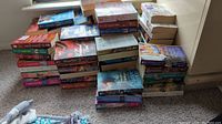 Multiple stacks of romance novels by various authors on carpet, showing 70 books in total
