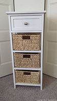 Front view of small white wooden table showing drawer and three wicker baskets
