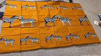 Full view of large orange tapestry with multiple black and white zebras in rows.