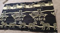 Photo of a black and white tapestry with multiple zebras and the word 'zebra' printed across it laid out on carpet.