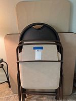 Stacked folding card tables and folded tan chairs showing beige tops and brown trim.