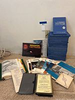 Photo showing a collection of blue National Defence manuals, Mission Vietnam book, Norton booklet, and other military magazines and manuals laid on carpet.