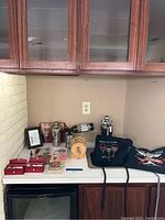 Wide view of bar accessories on counter including aprons, martini tool kit, wine stoppers, small barrel container, framed art and cocktail set