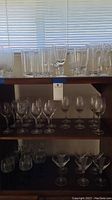 Shelf view showing an assortment of bar glasses, plastic glasses on top shelf and clear glassware below including wine and martini glasses.