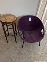 Full view of wooden cane barstool and mid century purple leather chair side by side on tile floor.