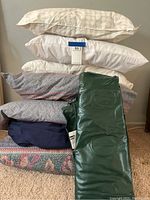 Stack of five pillows with assorted pillowcases in various colors and patterns including cream, white, floral and navy, along with blue bed skirt at bottom.