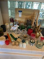 Candles, holders, and wooden cutting board arranged on a tiled surface near glass block window.