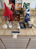 Photo showing cleaning sprays, Drano bottle, and several types of packaged and loose light bulbs arranged on a tiled counter.