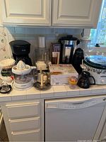 Overall view of kitchen appliances including coffee makers, blender, food processor, slow cooker, mixer, and cutting tool arranged on kitchen counter