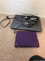 Laptop with cables on carpet, tablet with purple case in front