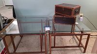 Two glass top tables side by side, decorative trunks on one table