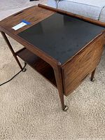 Front three-quarter view showing wood veneer top with black laminate inset, drop-leaf panel in closed position and lower shelf.