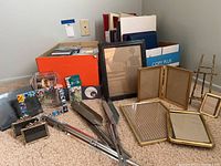 Box containing empty CD cases, assorted folders, framed empty frames, music stands, all laid on carpet