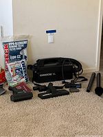 Photo showing handheld Oreck XL vacuum cleaner and several accessories including brush heads and hoses on carpet