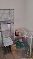 Photo showing the wire grid shelves stacked vertically with some plastic bins stacked nearby. The bins contain stuffed toys. Wire racks and a white utensil organizer are visible on the floor near the shelves.