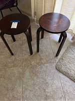 Two small round dark brown wooden tables on tiled floor near carpet and curtains.