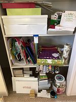 Shelf with assorted gift boxes, rolls of wrapping paper, various gift bags, and containers with ribbons