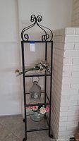 Full view of black wrought iron display shelf holding floral arrangements and lantern