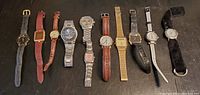 Photo of all 11 assorted wrist watches laid out in a row on a dark surface showing various bands and face styles.