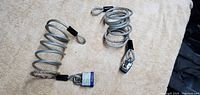 Two coiled steel lock safety cords on a light surface. One has a small padlock attached.