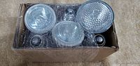 Top view of 5 halogen light bulbs, various shapes and clear glass, inside an open box wrapped with plastic wrap.