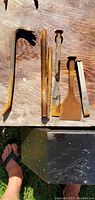 Six rusty metal hand tools arranged on wooden surface including two crowbars, two chisels, and two spikes