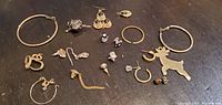 Assorted fine jewelry laid out flat on dark surface including hoops, studs, and charm in good shape.