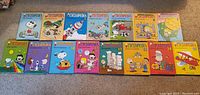 Photo showing all 15 volumes of Charlie Brown's Encyclopedia laid out side-by-side, showcasing colorful illustrated covers with Peanuts characters.