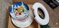Photo of the Disney 1985 Christmas collector plate inside its packaging showing the front design with Mickey Mouse and Pluto with presents in a snowy scene.