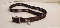 Full length view of the brown woven leather belt laid out showing the buckle end with Fossil brand stamped on it.