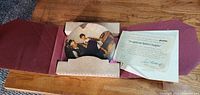 Opened box with collectible plate depicting Norman Rockwell artwork and accompanying certificate of authenticity, plate partially wrapped.