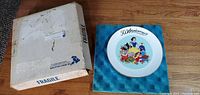 Photo of the collectible Disney 50th Anniversary plate displayed on a blue padded case next to its original fragile box.