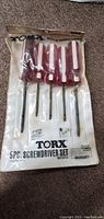 Photo of Torx screwdriver set packaged in original clear sealed plastic with red handles and metal shafts visible.