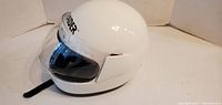 Side angled view of white Raider motocross helmet with clear visor and black strap.