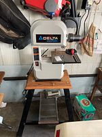 Front view of the white Delta ShopMaster 9" bench band saw on a wooden top mounted on a heavy black stand.
