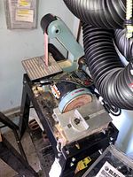 Front and side view of Delta belt and disc sander mounted on black metal work table with sanding belts below.