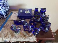 Top-down view of all eight Fenton glass items on lace cloth and wooden table