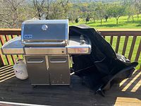 Full view of grill assembled on deck with propane tank at left and folded cover at right