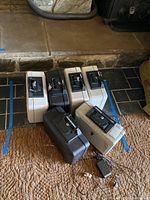 Photo showing six Sentry safe boxes in black and off-white colors on floor with locks and keys visible, one power adapter in foreground.