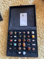 Black hinged ring box open showing rings displayed in foam tray