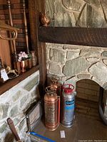 The lot arranged beside a fireplace hearth showing all fire extinguishers and copper pot together for scale and detail.