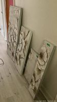 Four matching floral canvas paintings arranged leaning against wall showing size variations and detail