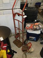 Rusty orange older hand cart with two solid wheels and flat base plate, missing one smaller wheel, items placed near freezer and other storage items