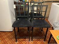 Four matching black metal frame chairs with padded suede-like seats shown in basement setting on patterned carpet.