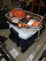 Blue and white wheeled Coleman cooler with black handle, orange boat safety kit with accessories inside a clear plastic bag on top.