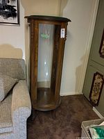 Front view of the wooden display cabinet with curved glass and carved wood frame next to a sofa.
