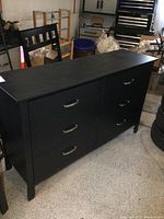 Front view of modern black dresser with six drawers and silver handles.