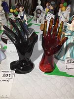 Both black and red glass hand sculptures placed side by side, with other ceramic figurines in background.