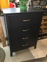 Front view of the modern black highboy dresser showing four drawers with curved metal handles.